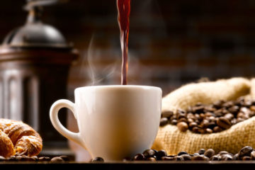 Tasse Kaffee im Setting zwischen Kaffeebohnen und Kaffeemühle