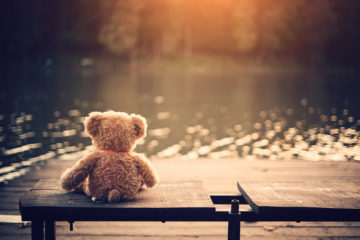 Teddy Bär sitzt einsam auf einer Bank an einem See