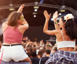 Musikfestivals 2024- Zwei junge Frauen sitzen auf den Schultern von Freunden lachend an einem Konzert.